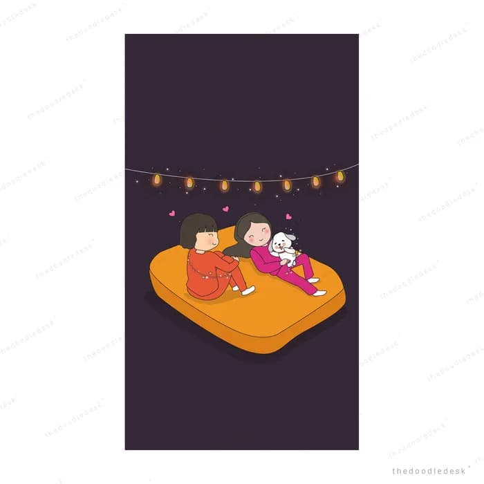 Two girls lying on an orange mattress with a cat under a string of lanterns
