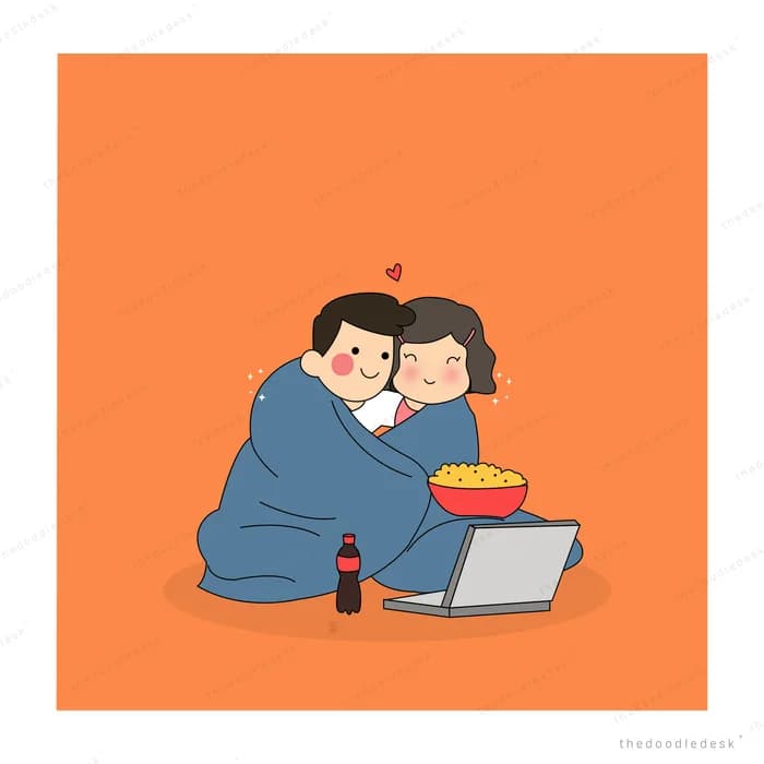 Couple sharing popcorn watching a laptop under a blanket
